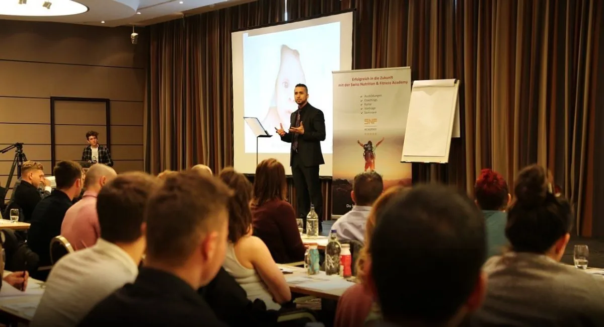 Birol Isik spricht auf der Bühne eines Seminars zu den Teilnehmenden